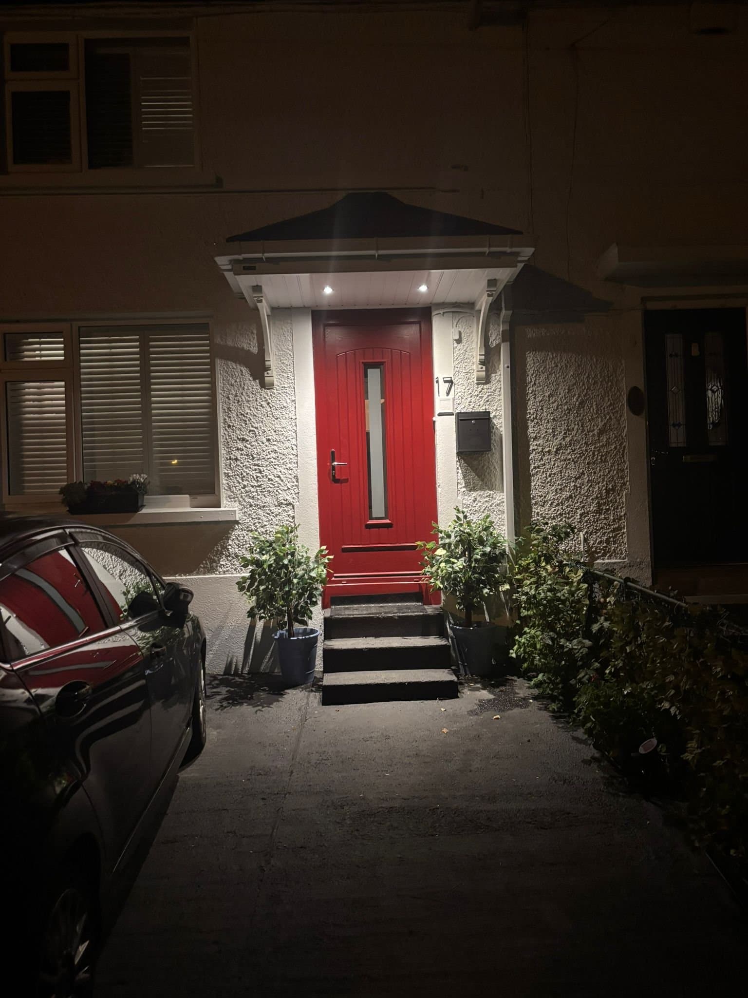 White hipped canopy with downlights illuminating red front door at night
